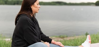Woman meditating outdoors by a tranquil lakeside, fostering health and wellness.